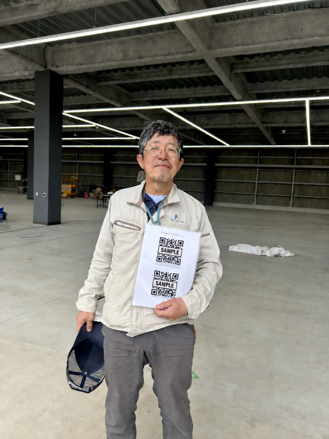 建設現場でQRコード付きの案内を手にしている様子。QRコードはSAMPLE入りの掲載用ダミーに差し替えています